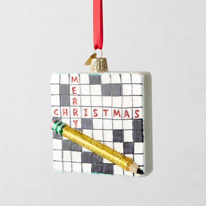 Square glass crossword puzzle ornament with "Merry Christmas" in red glitter and a gold glitter pencil.