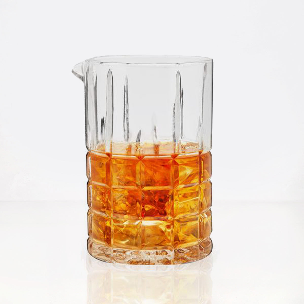 Clear square-cut crystal cocktail mixing glass with a pour spout, filled with amber liquid and ice.