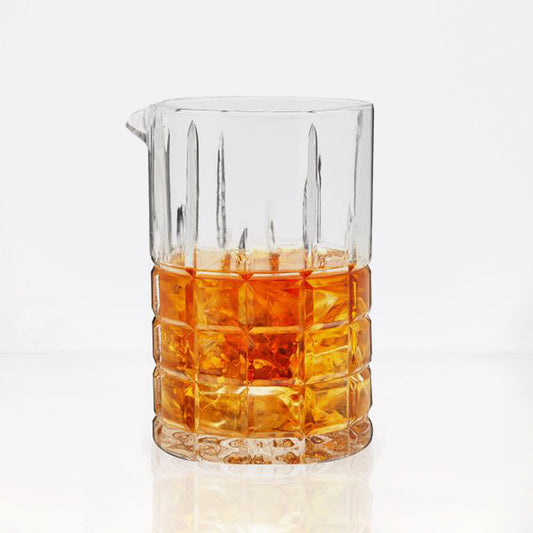 Clear square-cut crystal cocktail mixing glass with a pour spout, filled with amber liquid and ice.