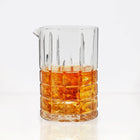 Clear square-cut crystal cocktail mixing glass with a pour spout, filled with amber liquid and ice.