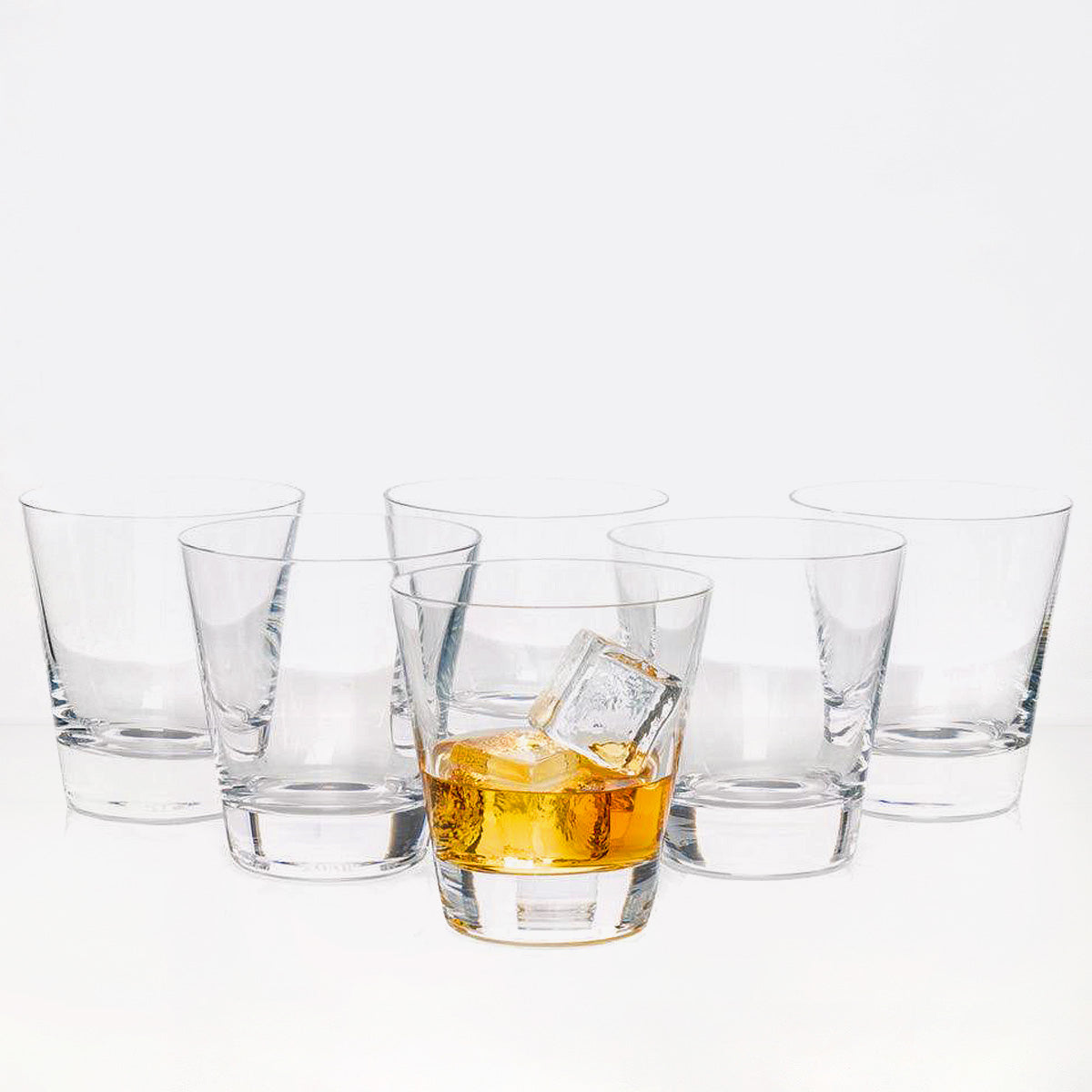 Set of 6 clear crystal whiskey glasses, one with amber liquid and ice.