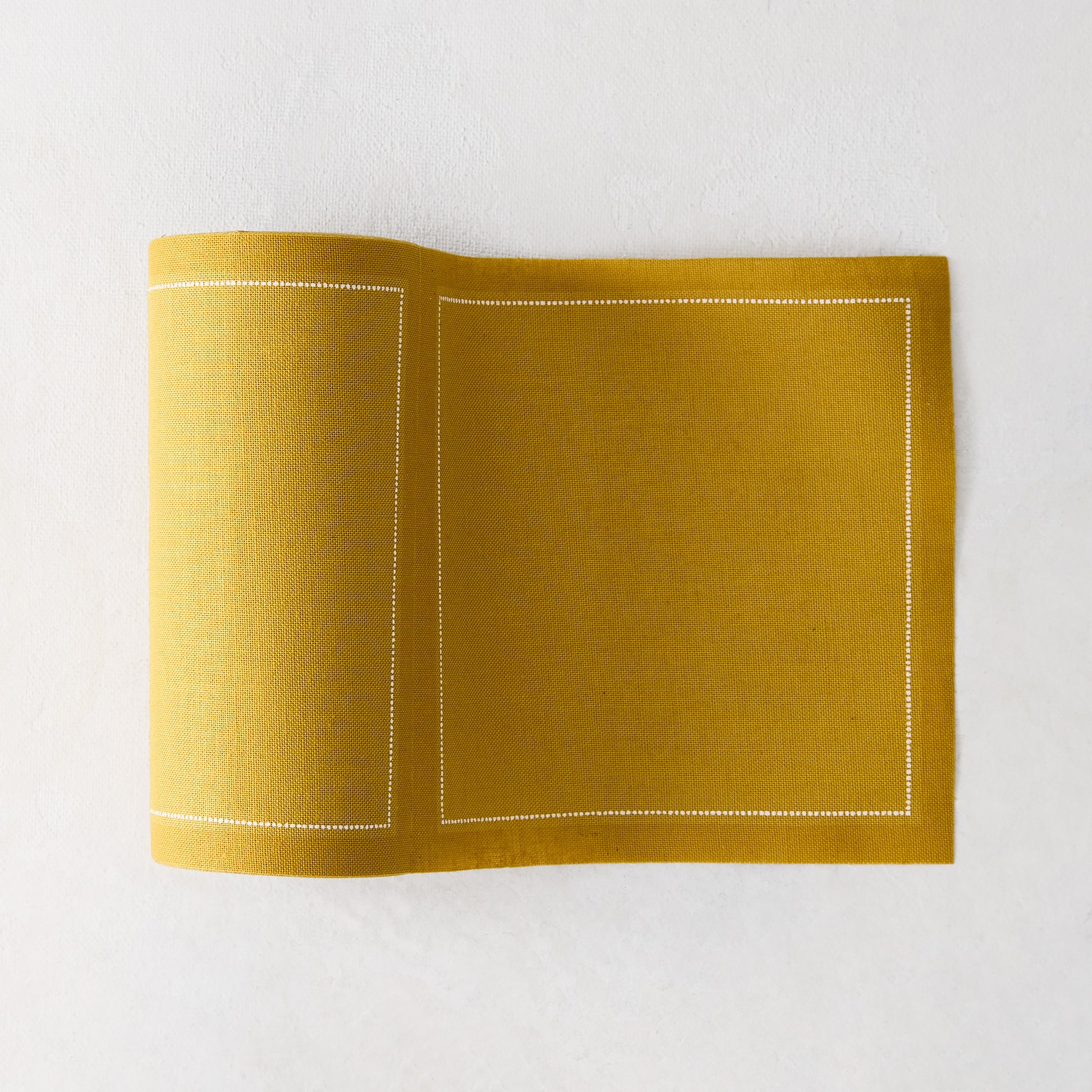 Curry yellow tear-off cotton cocktail napkin roll with white dotted border, partially unrolled.