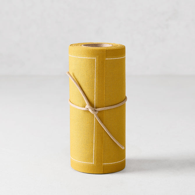 Roll of 50 Curry Yellow cotton tear-off cocktail napkins with white stitched borders, tied with twine.