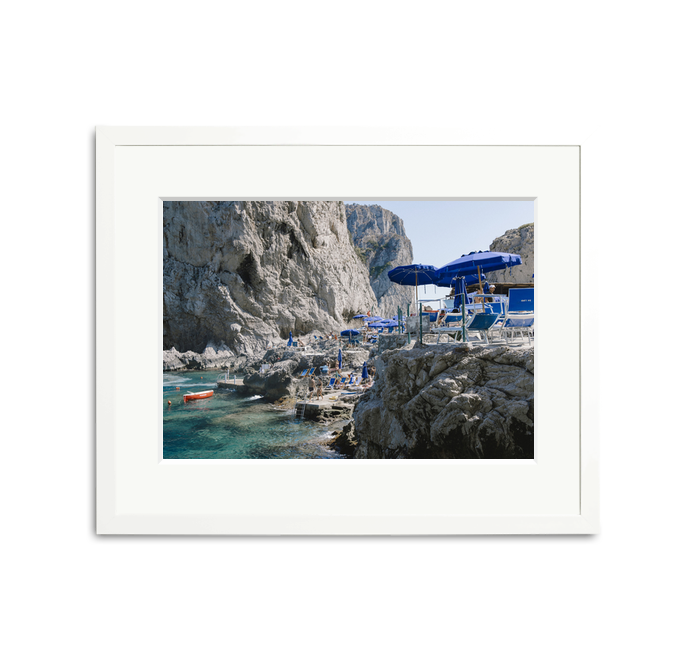 Da Luigi Ai Faraglioni framed wall art print with blue umbrellas, beachgoers, and clear water.