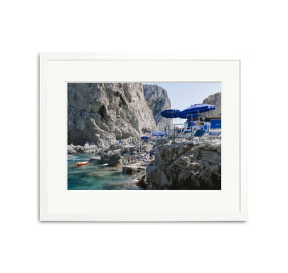 Da Luigi Ai Faraglioni framed wall art print with blue umbrellas, beachgoers, and clear water.