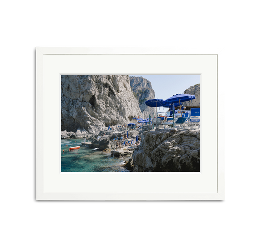 Da Luigi Ai Faraglioni framed wall art print with blue umbrellas, beachgoers, and clear water.