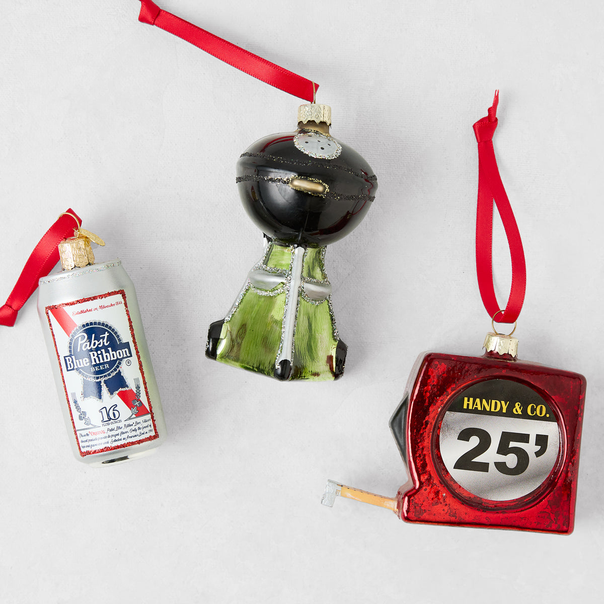 Glass ornament set featuring a PBR beer can, black grill, and red 25-foot measuring tape with red hanging ribbons.