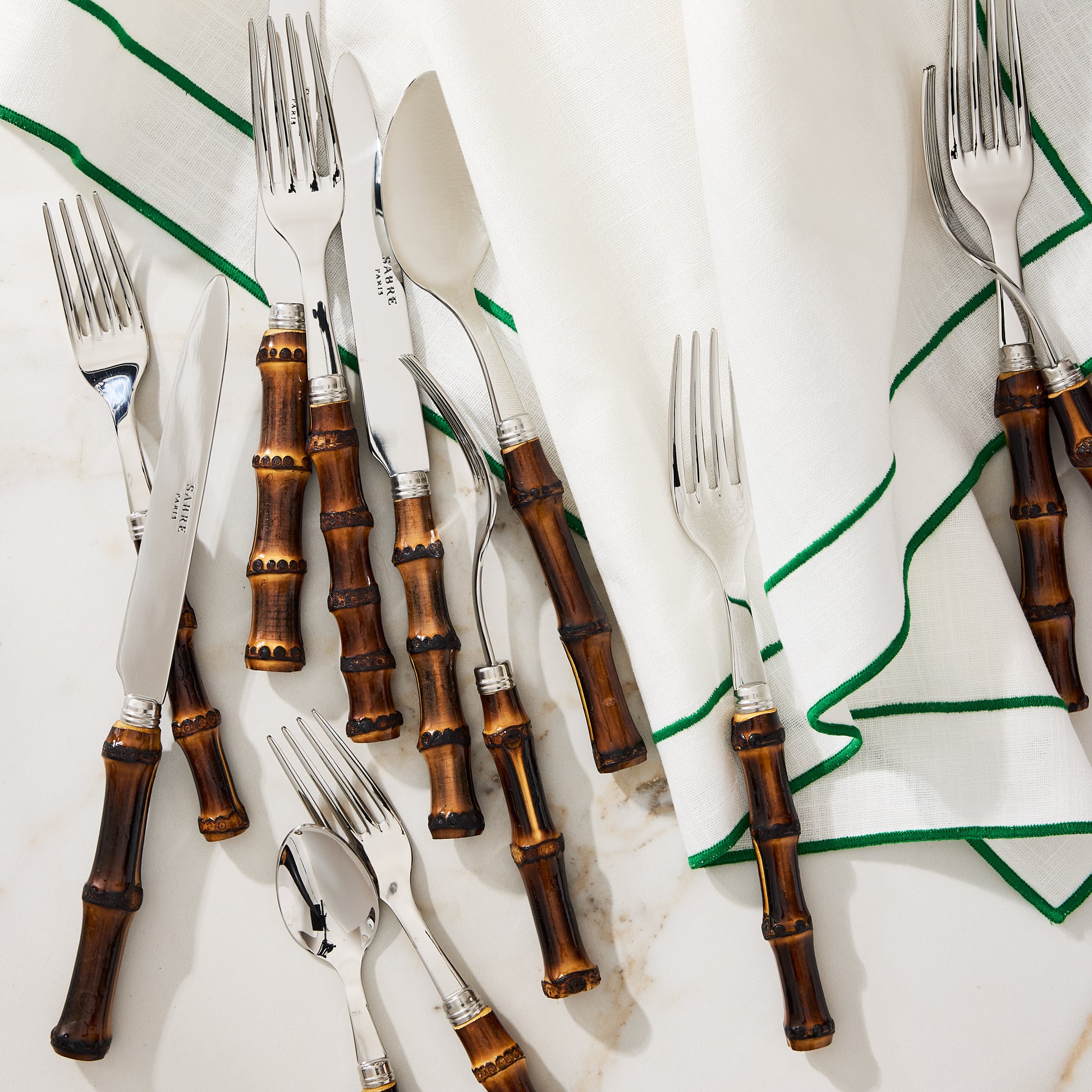 Dark bamboo 5-piece flatware set with stainless steel utensils and a white napkin with green trim.