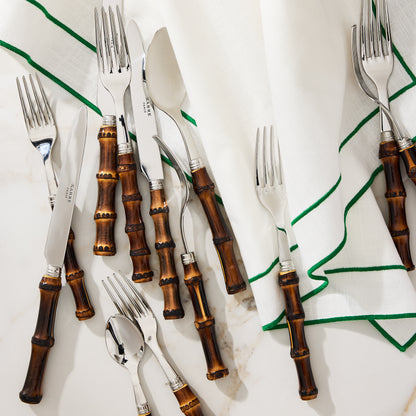 Dark bamboo 5-piece flatware set with stainless steel utensils and a white napkin with green trim.