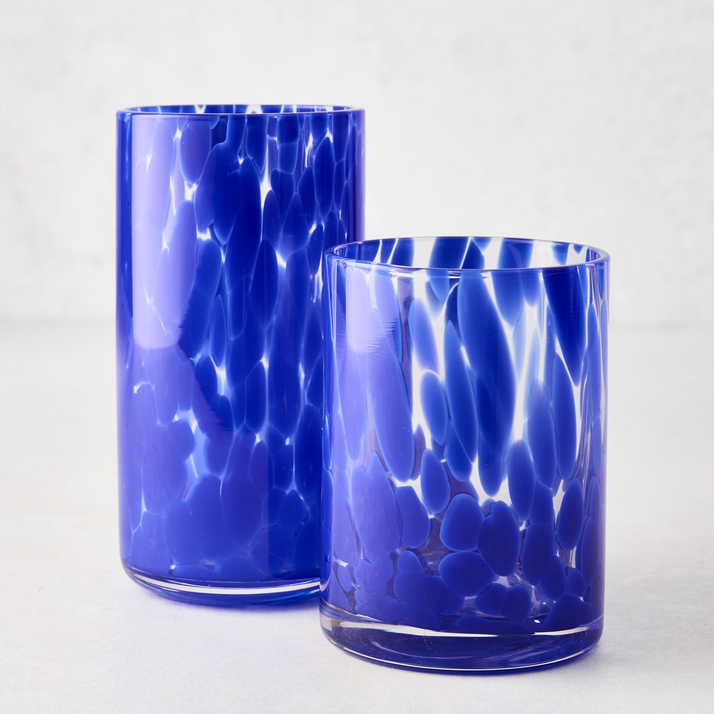 Two dark blue spotted glass highball and rocks glasses on a white surface.