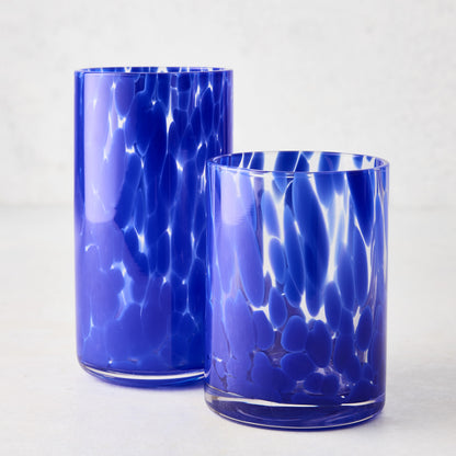 Two dark blue spotted glass highball and rocks glasses on a white surface.