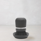 Dark grey soap dispensing dish brush with polyester bristles and clear reservoir on a matching stand.