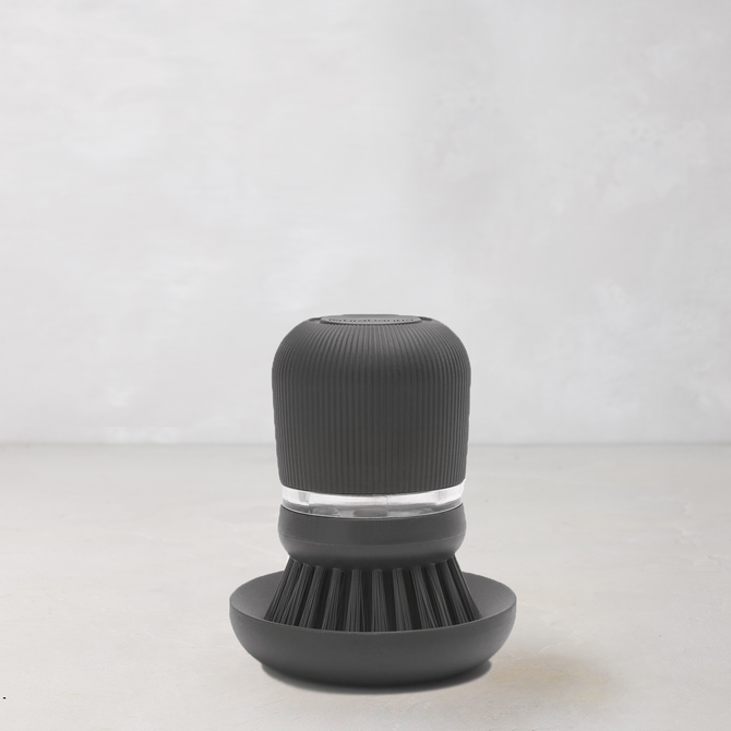 Dark grey soap dispensing dish brush with polyester bristles and clear reservoir on a matching stand.