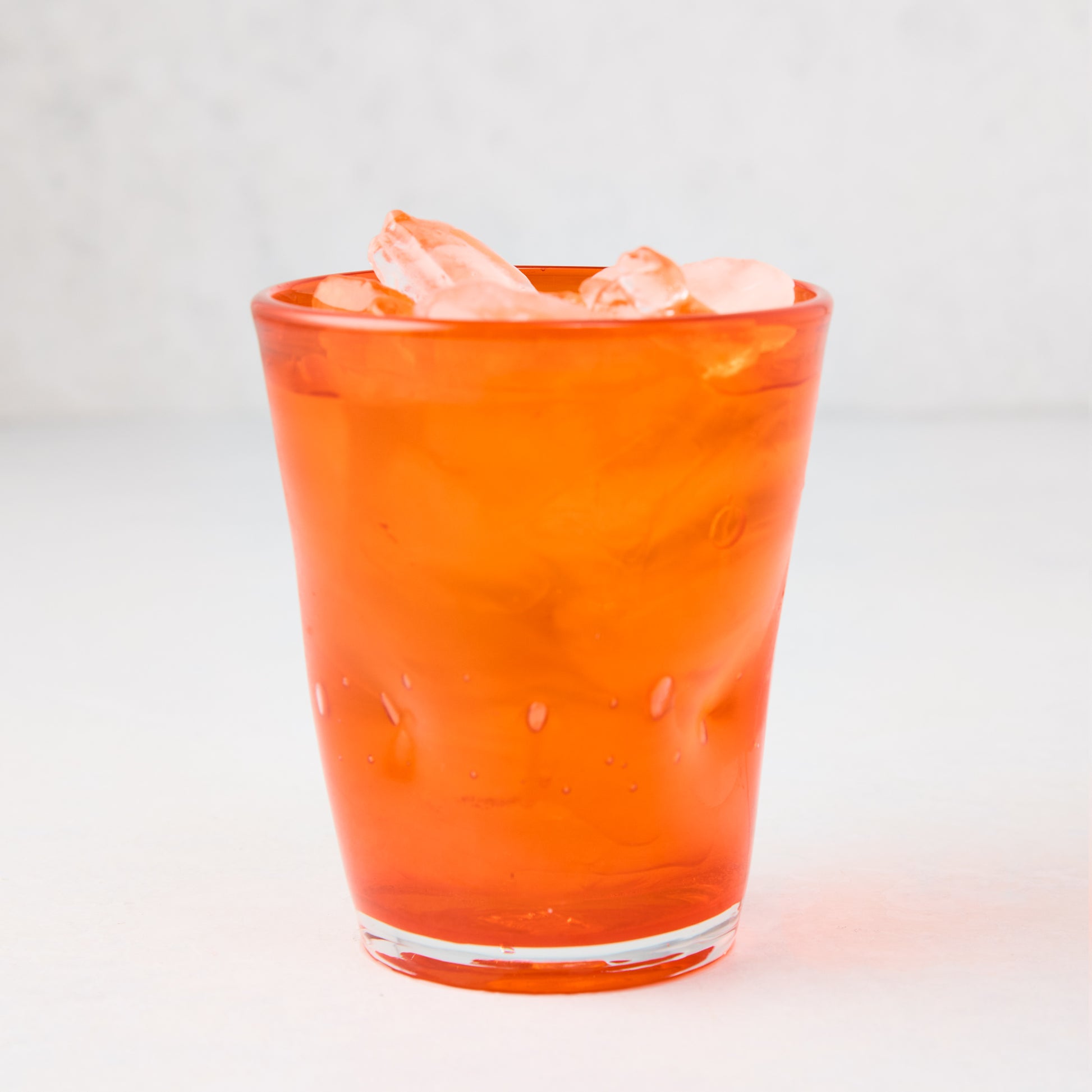 Dark orange Henri mouth-blown glass, 8 oz, filled with ice.