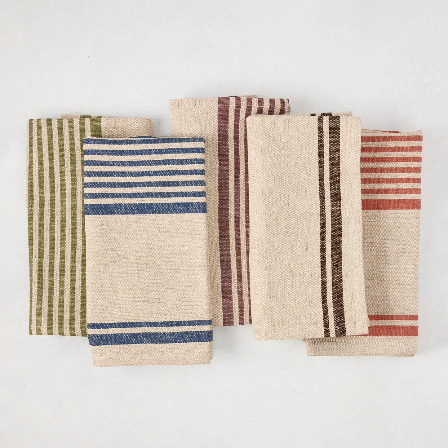 Five folded linen-cotton napkins with beige bases and stripes in dark plum, blue, green, brown, and rust.