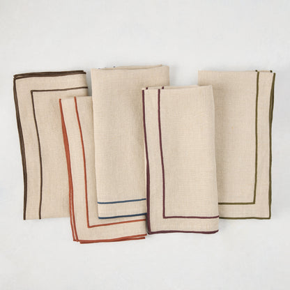 Beige cotton napkins with dark plum, brown, blue, orange, and olive green embroidered double line borders.
