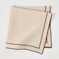 Beige cotton napkin with dark plum embroidered double line border, folded.