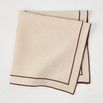 Beige cotton napkin with dark plum embroidered double line border, folded.