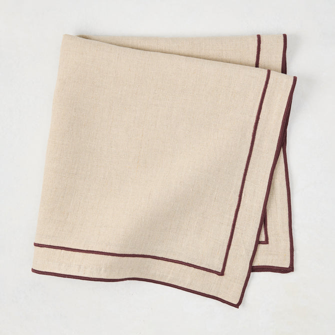 Beige cotton napkin with dark plum embroidered double line border, folded.