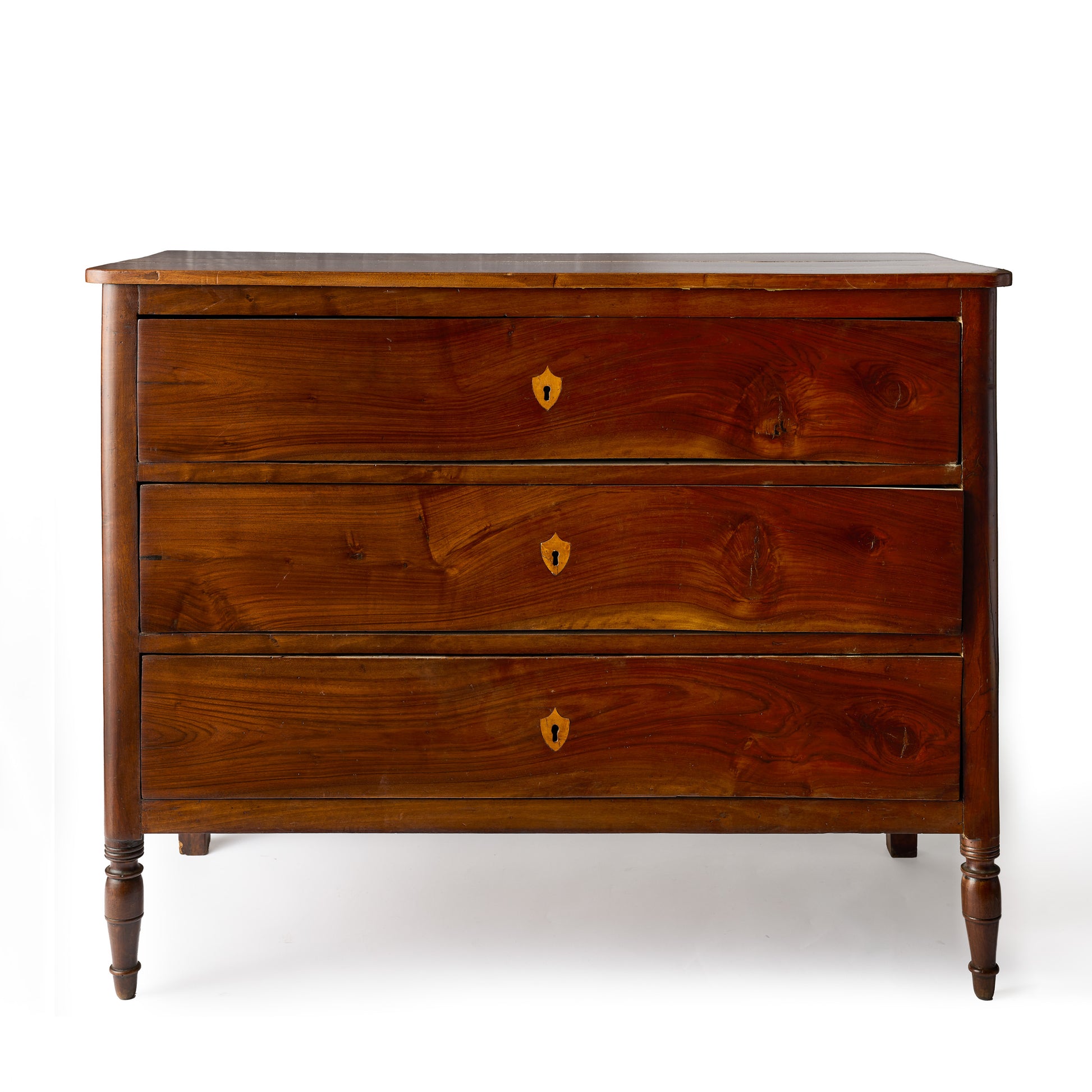 Dark wood dresser with three drawers, mahogany veneer, brass keyholes, and turned feet in a French empire style.