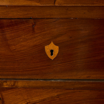 Dark mahogany wood dresser drawer front with a decorative brass shield-shaped keyhole inlay.