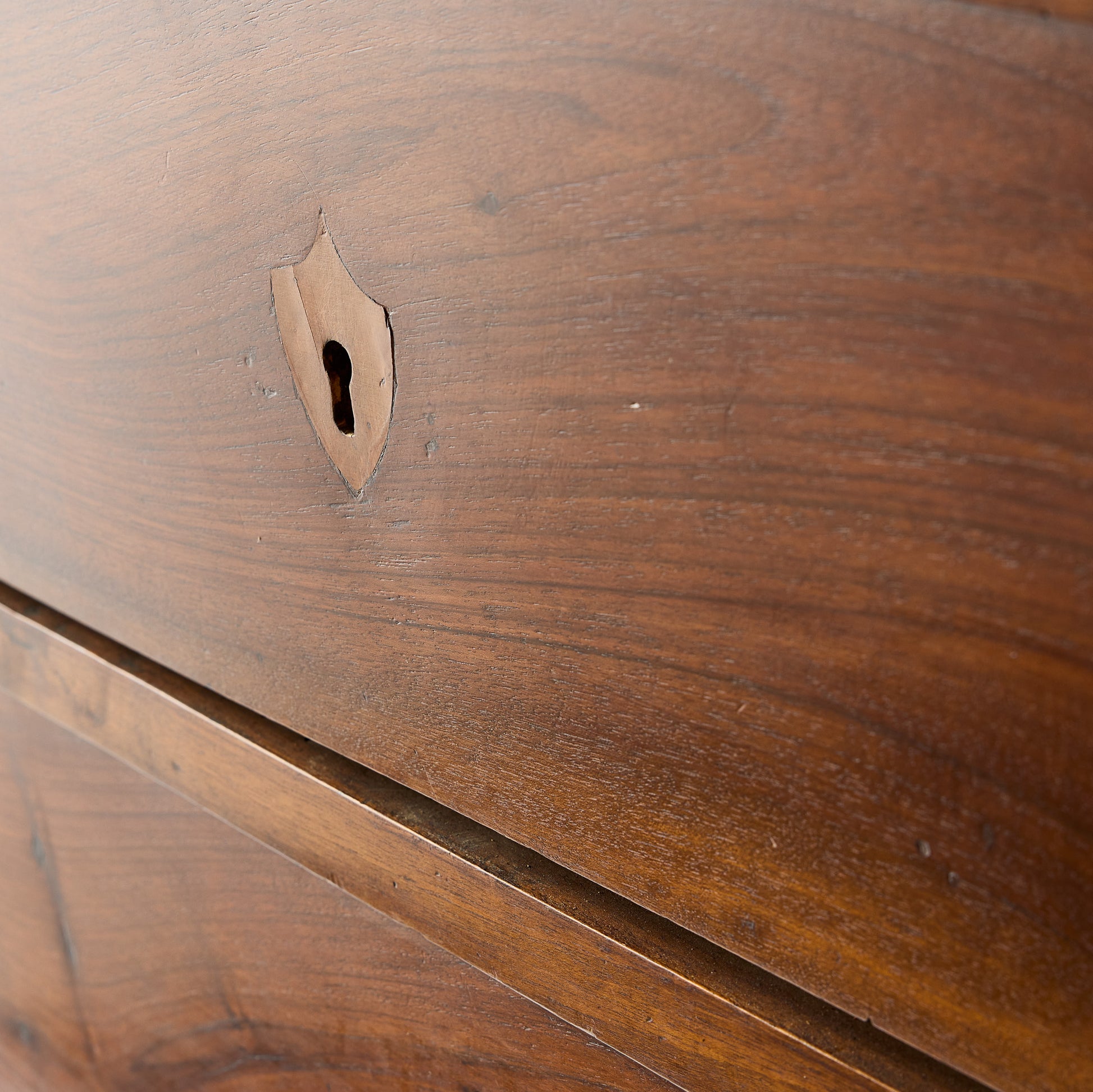 Close-up of a dark mahogany wood dresser drawer featuring an original brass keyhole in a French empire style.