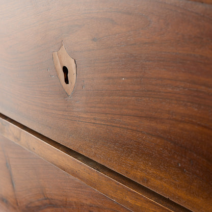 Close-up of a dark mahogany wood dresser drawer featuring an original brass keyhole in a French empire style.