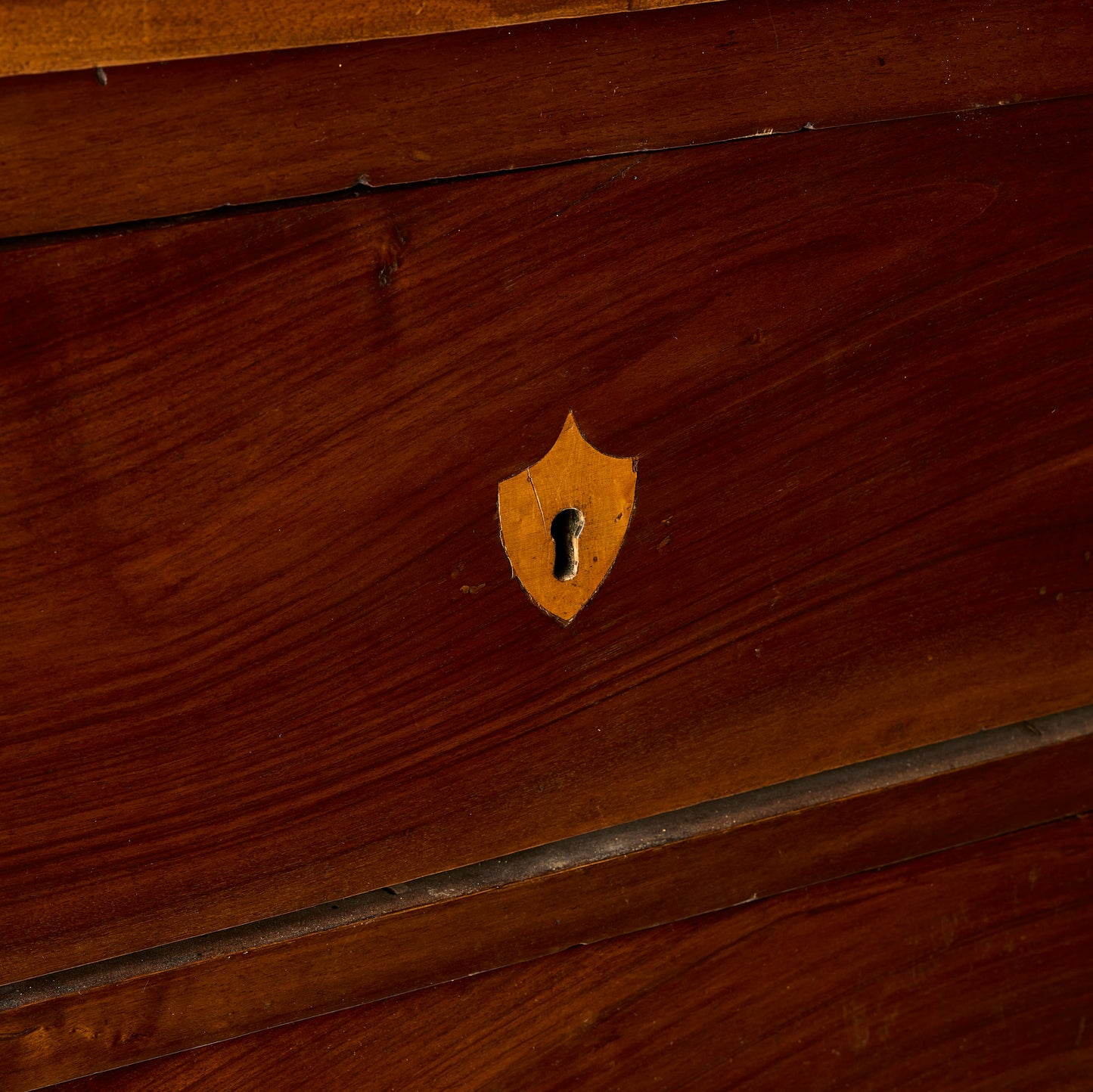 Dark mahogany wood dresser drawer featuring an inlaid brass shield-shaped keyhole escutcheon.