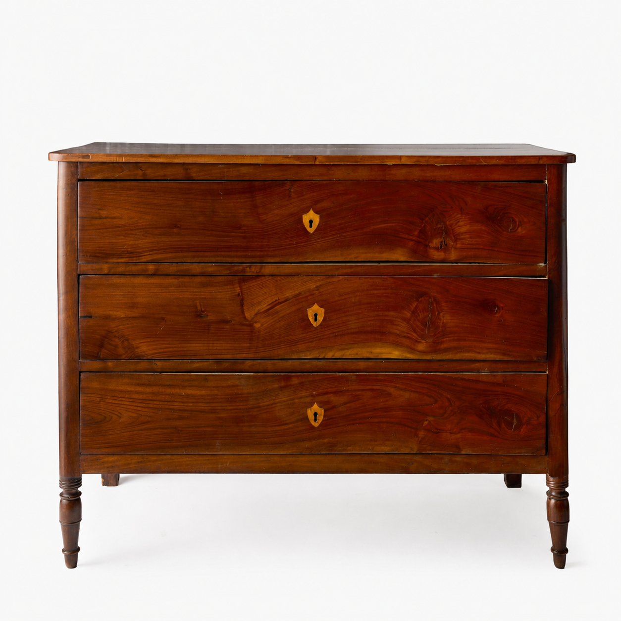 Dark mahogany wood dresser with three drawers, brass keyholes, and turned feet in a French Empire style.