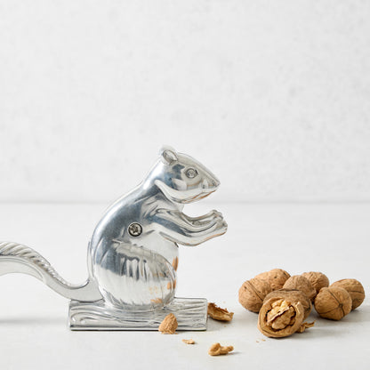 Silver squirrel-shaped metal nutcracker with a pile of whole walnuts on a white surface.