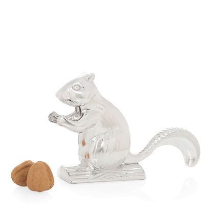 Shiny silver metal squirrel nutcracker with two walnuts beside it.