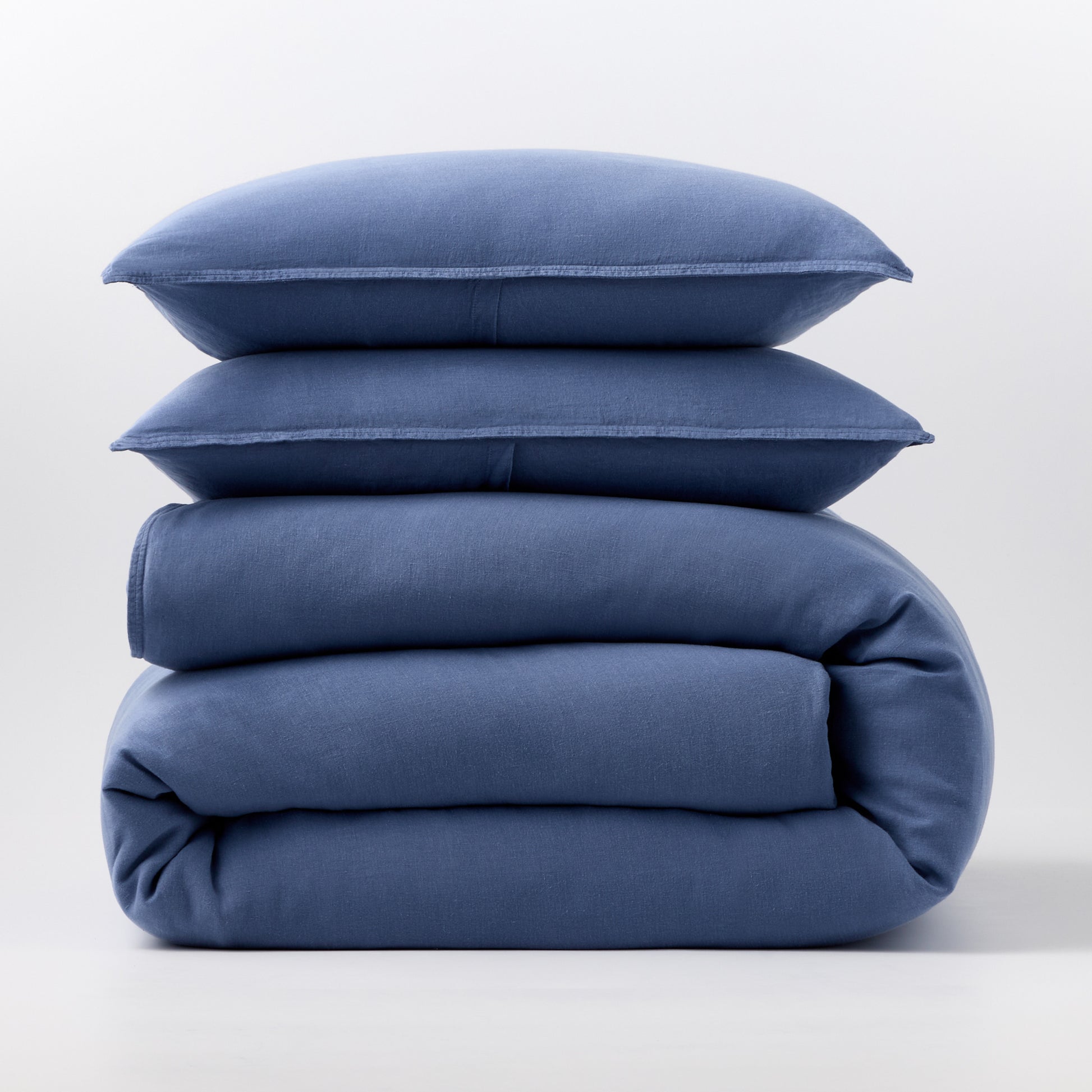 Stacked denim blue European washed linen duvet cover and two matching pillow shams on a white background.