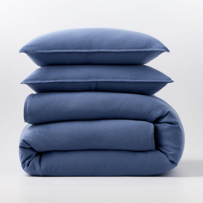 Stacked denim blue European washed linen duvet cover and two matching pillow shams on a white background.