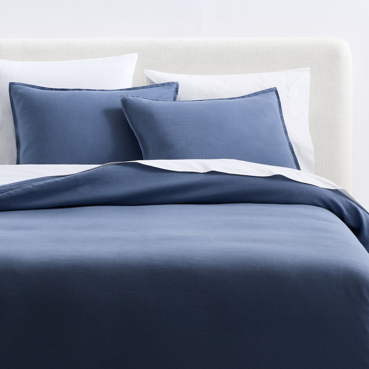 Set of two denim blue European washed linen euro shams on a bed with white pillows and a matching blue duvet cover.