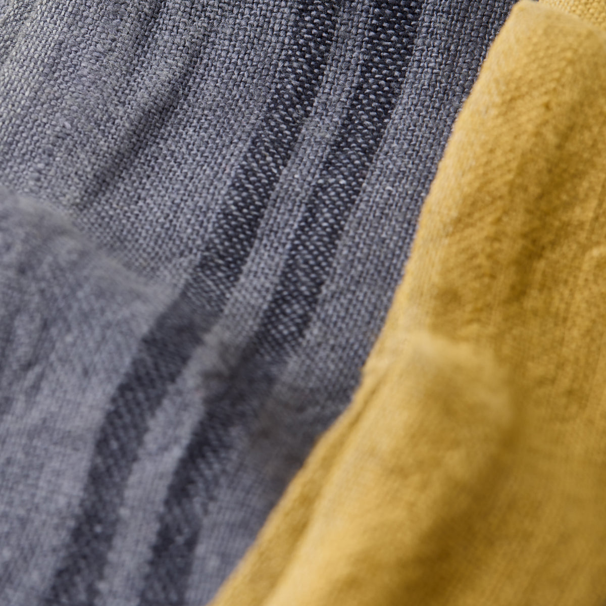 Close-up of a denim blue striped linen tea towel next to a solid yellow linen towel.