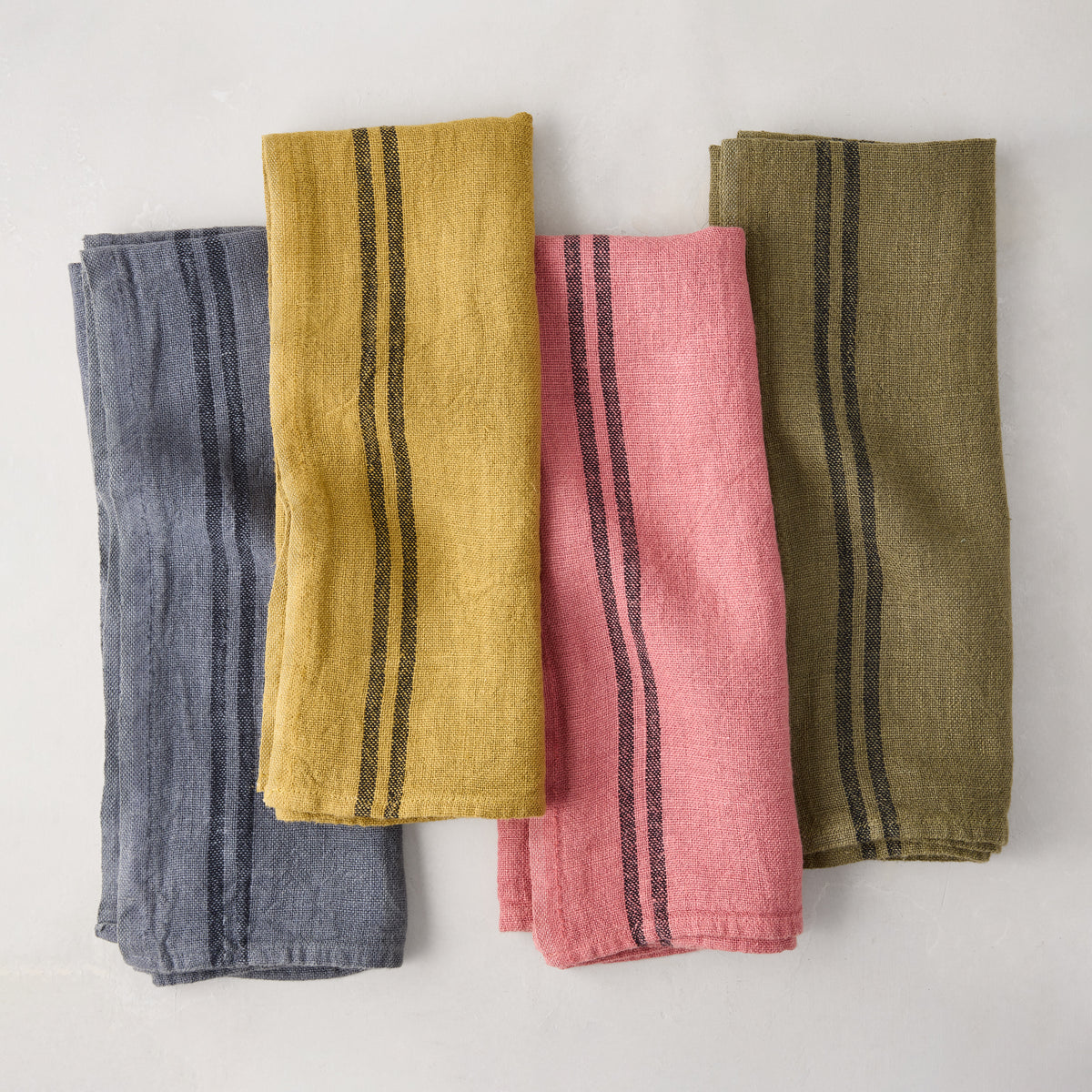 Four folded linen tea towels: blue, yellow, pink, and olive green, each with black stripes.
