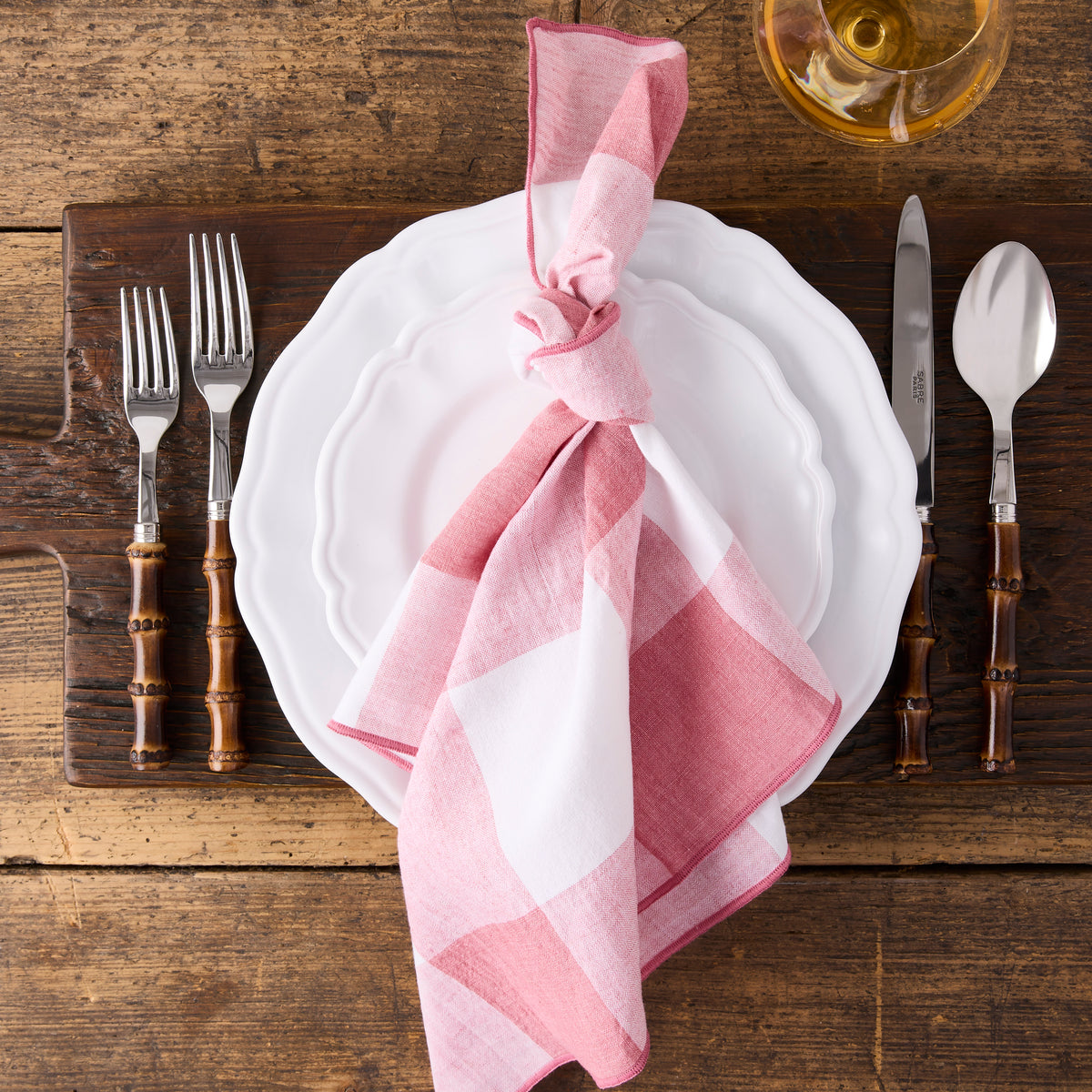 11-inch white ceramic Deruta dinner plate with scalloped edges, topped with a pink and white checkered napkin.