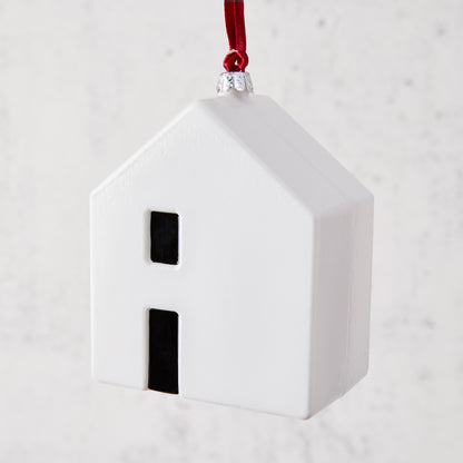 White ceramic house ornament with black windows, hanging from a red ribbon.