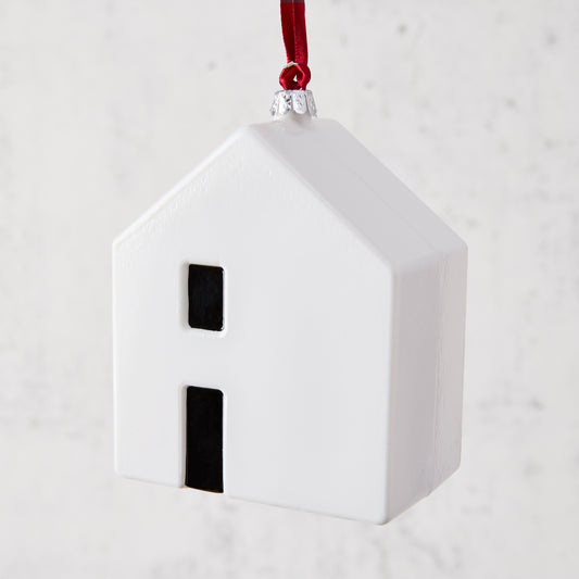 White ceramic house ornament with black windows, hanging from a red ribbon.