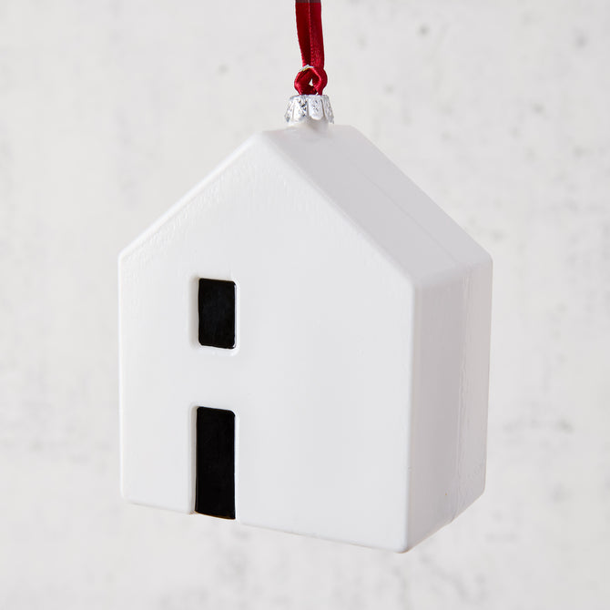 White ceramic house ornament with black windows, hanging from a red ribbon.