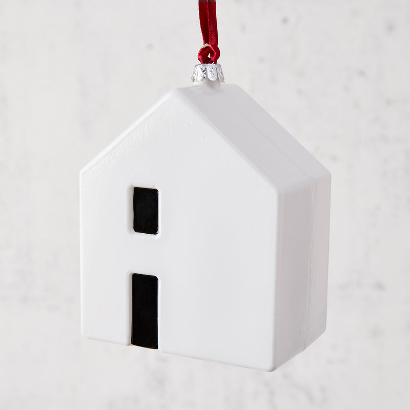 White ceramic house ornament with black windows, hanging from a red ribbon.