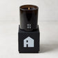 Diane Keaton x Hudson Grace "HOUSE" scented candle in a sleek black glass vessel on a black gift box with a house logo.
