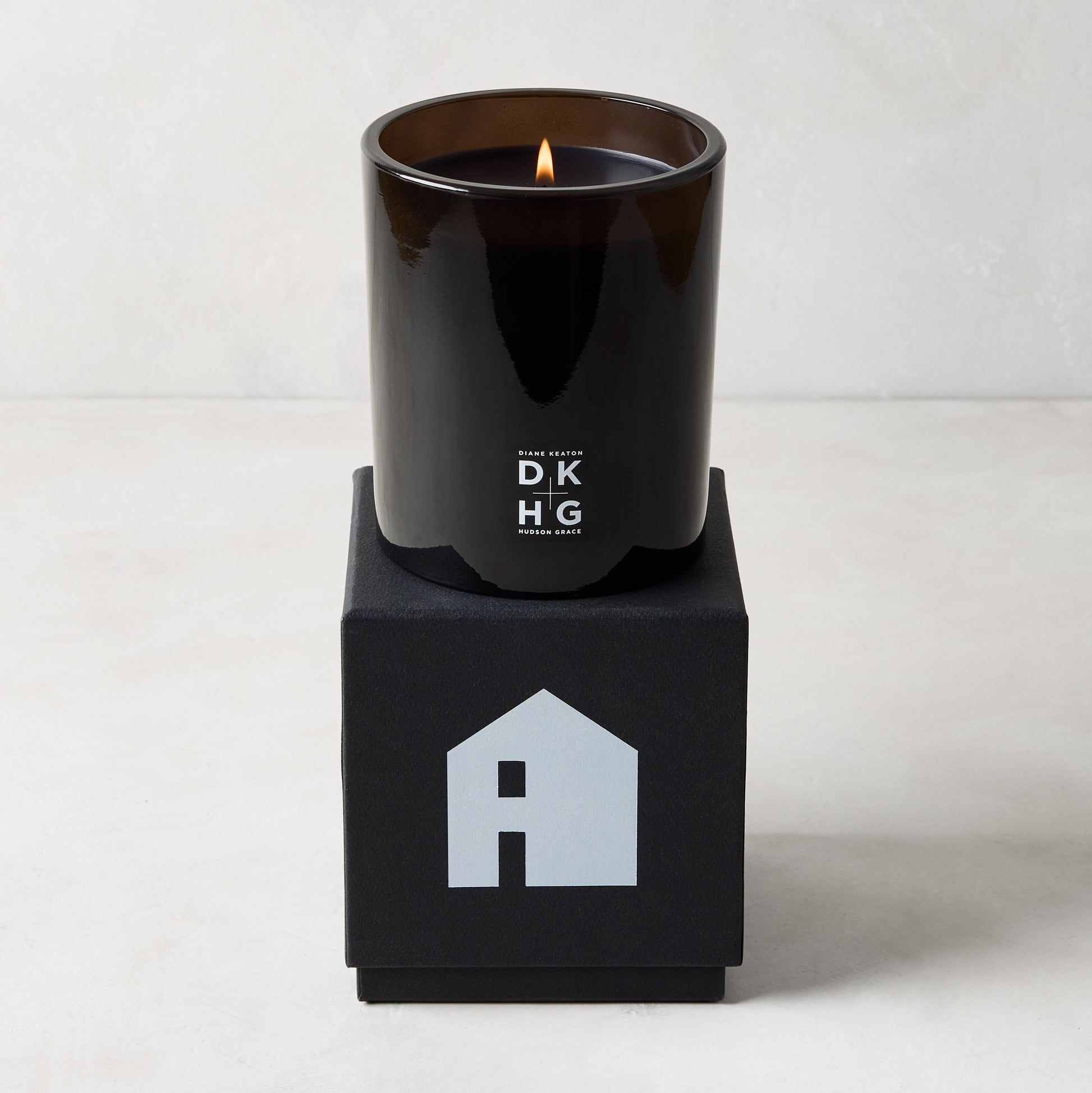 Diane Keaton x Hudson Grace "HOUSE" scented candle in a sleek black glass vessel on a black gift box with a house logo.