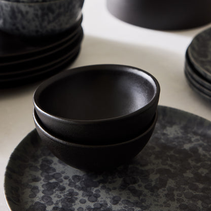 Two stacked Diane Keaton + Hudson Grace matte black graphite stoneware individual bowls on a speckled plate.