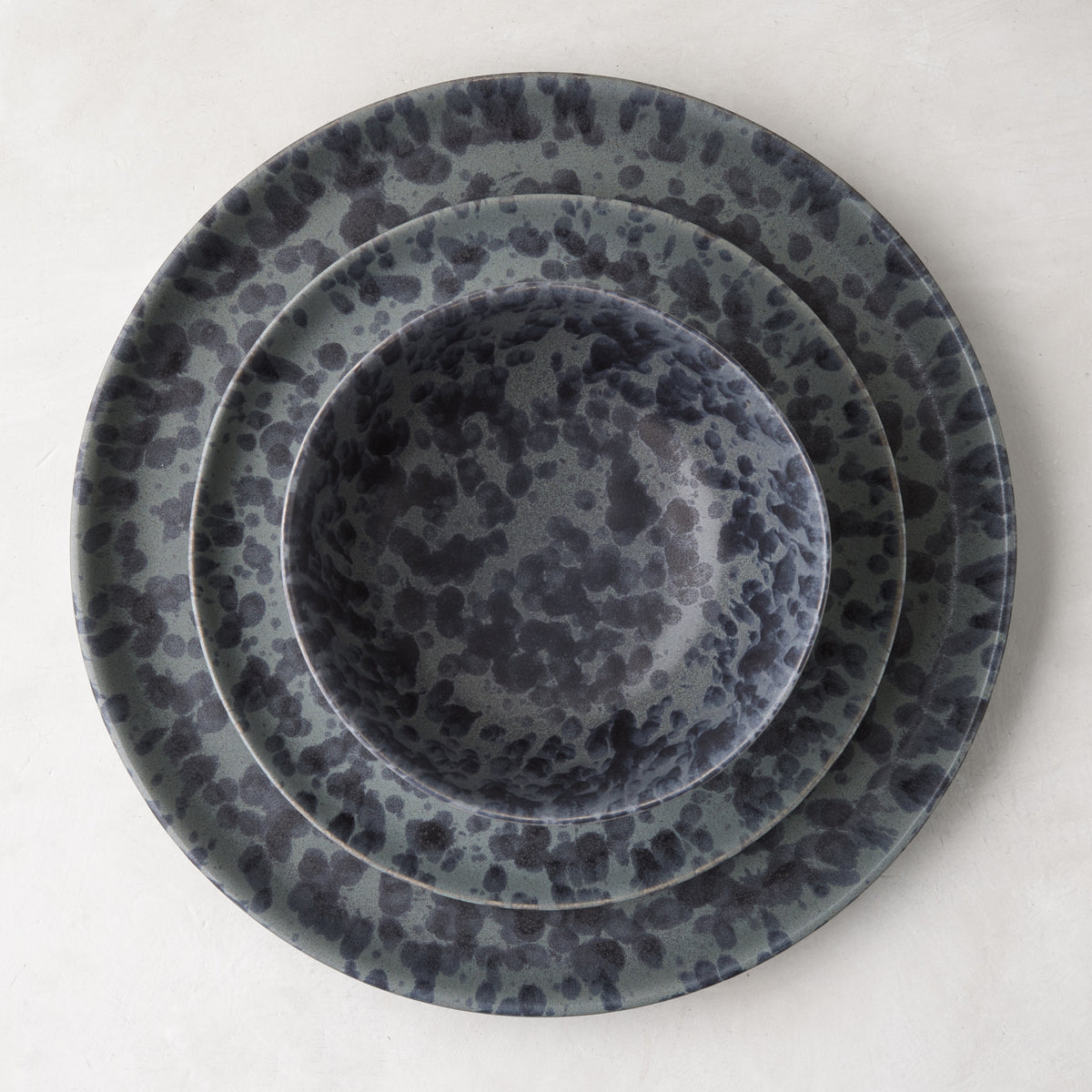 Diane Keaton + Hudson Grace Composition Splatter Stoneware Bowl, black and grey, nested on two matching plates.