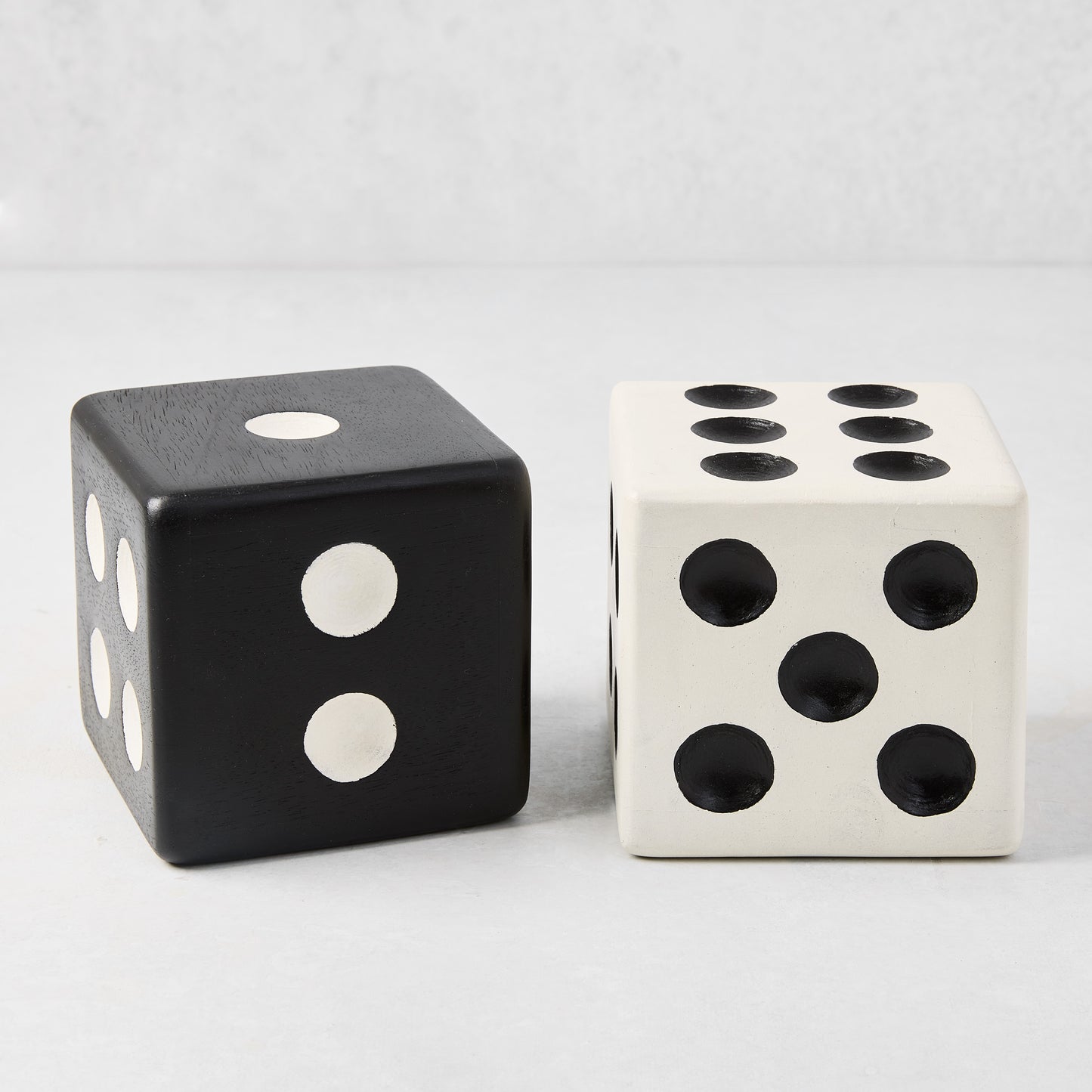 Two Diane Keaton + Hudson Grace decorative carved mango wood dice: one black with white dots, one white with black dots.
