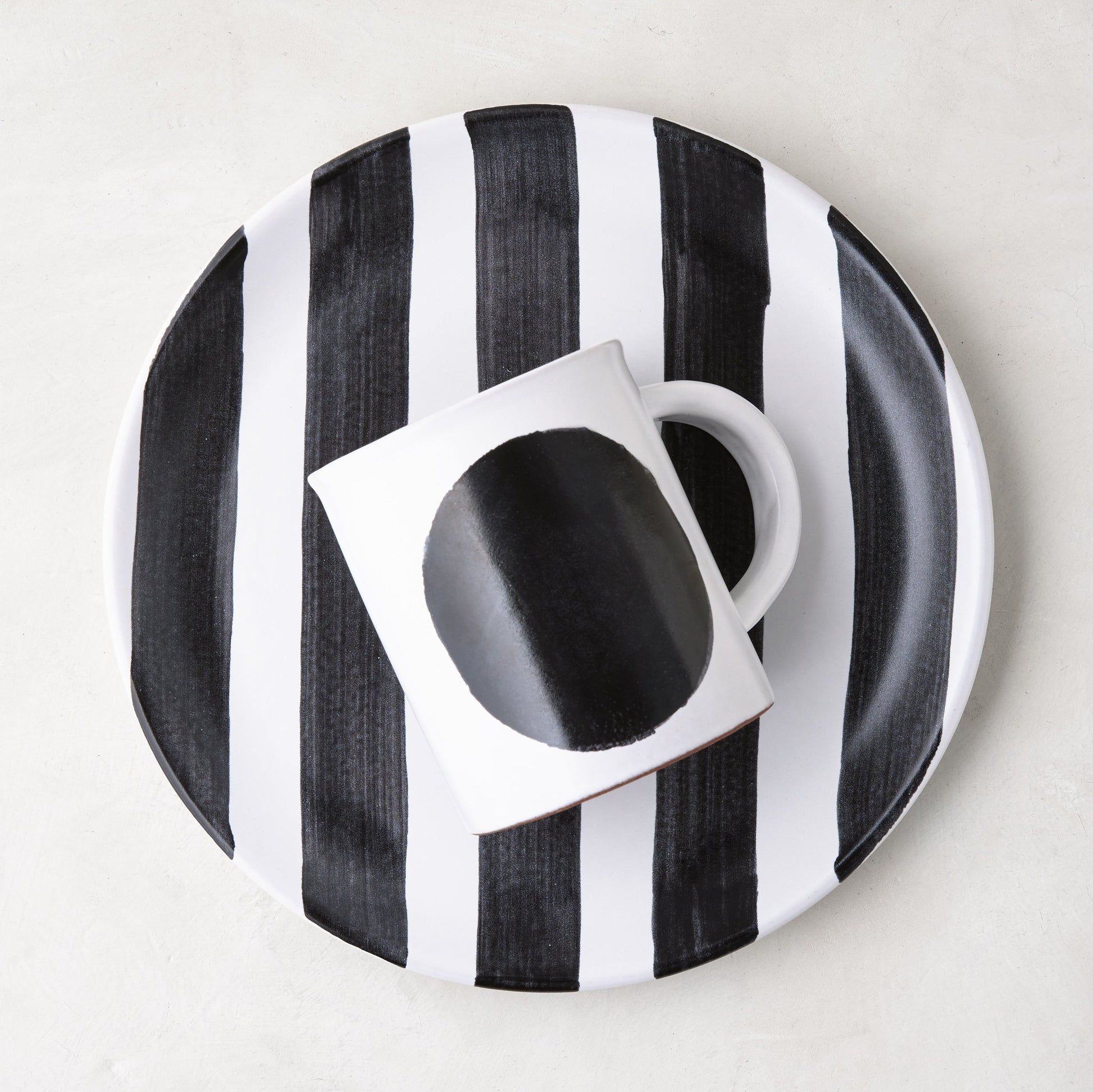 Diane Keaton + Hudson Grace Domino Dot Stoneware Mug with a bold black circle, on a striped plate.