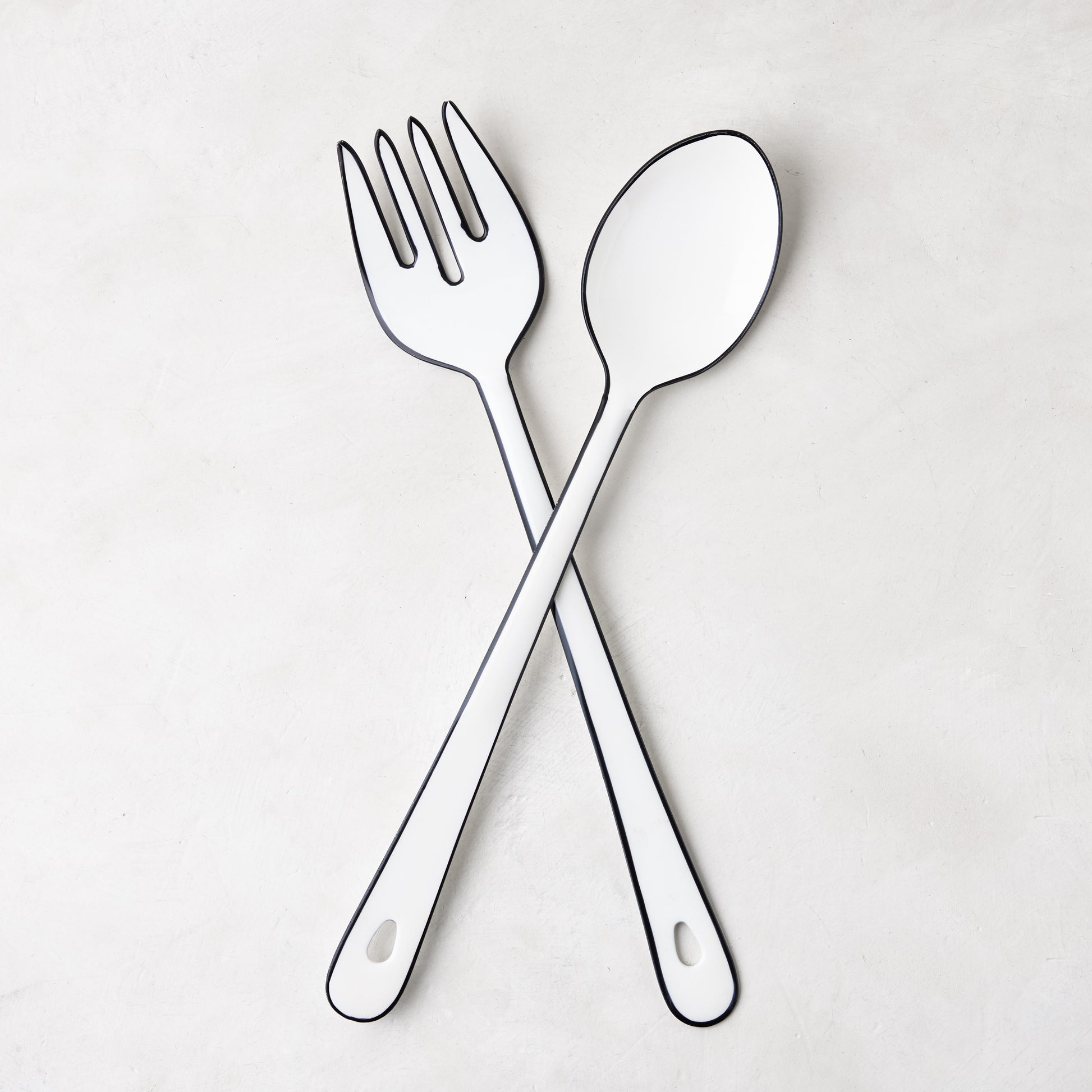 Diane Keaton + Hudson Grace white enamel serving fork and spoon with black borders, crossed.