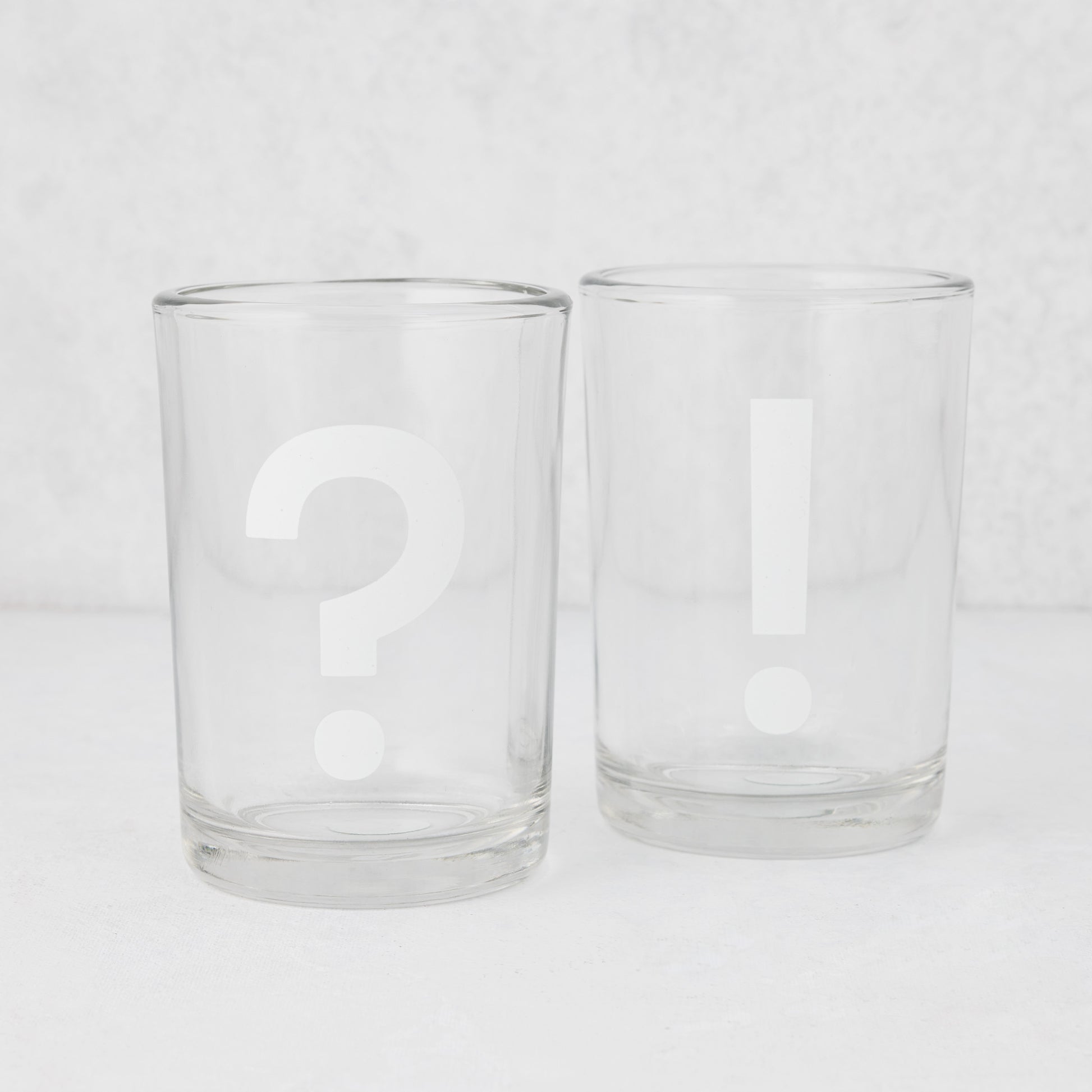 Two clear glass tumblers, one with a white question mark, one with a white exclamation point.