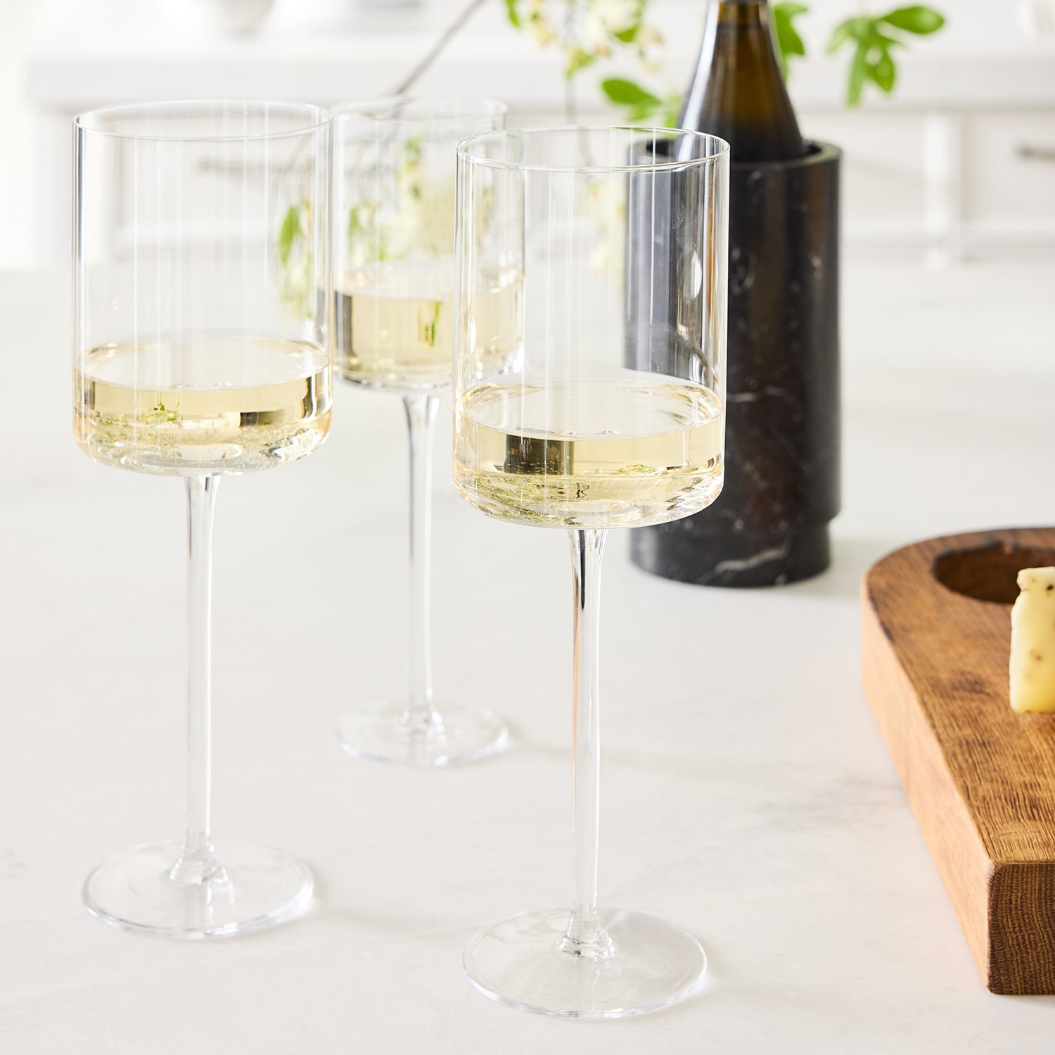 Three clear, tall Diane Keaton + Hudson Grace High Rise Small Wine Glasses filled with white wine.